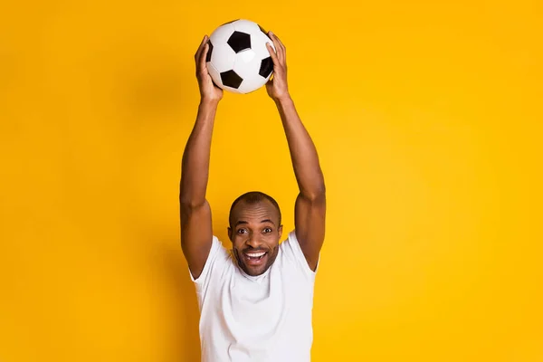 Восхитительный позитивный веселый афро-американец парень провести футбольный мяч праздновать гол сборной мира по футболу матч носить белую футболку изолированы над ярким блеском желтый цвет фона — стоковое фото
