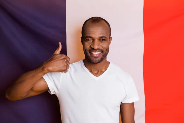 魅力的な黒い肌の男の写真フランス国旗立っている男良い気分親指を上げるカジュアル白いTシャツを着用隔離された3色の旗の背景 — ストック写真