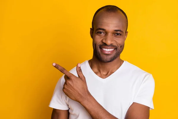 Close-up foto van aantrekkelijke donkere huid man regisseren vinger kant lege ruimte tonen nieuwigheid informatie quarantaine dragen casual wit t-shirt geïsoleerde heldere gele kleur achtergrond — Stockfoto