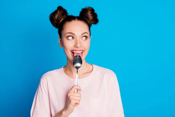 Photo of pretty lovely lady two funny buns metal spoon inside mouth lick try tasty meal tricky look side empty space wear casual pink t-shirt isolated bright blue color background