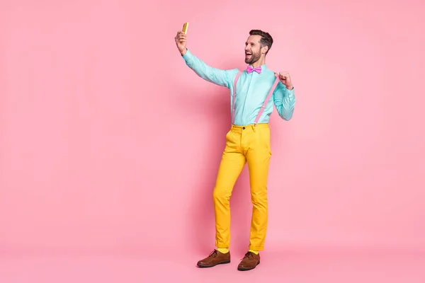 Foto de comprimento total de bonito cara tendência roupas navegação telefone gravação vídeo para blog post desgaste camisa suspensórios arco gravata calças amarelas sapatos isolado pastel cor rosa fundo — Fotografia de Stock