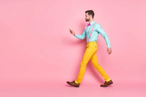 Full size profile side photo of serious focused guy blogger go walk copyspace use cellphone read social network news post wear trousers shoes shirt isolated pastel color background