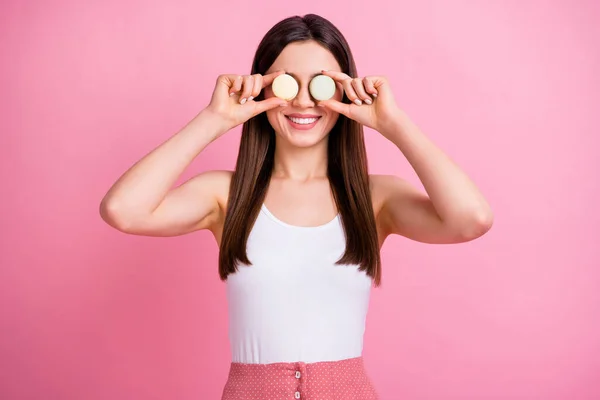 Фото очаровательной забавной леди держать два печенья макарон скрывая глаза, как спецификации игривое настроение носить белый синглет пунктирная юбка изолированные пастельно-розовый цвет фона — стоковое фото