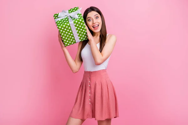 Foto de encantadora señora divertida mantenga grandes verdes punteado arco caja de regalo manos tratar de adivinar lo que en el interior usan blanco singlet corto punteado falda aislado pastel rosa color fondo —  Fotos de Stock