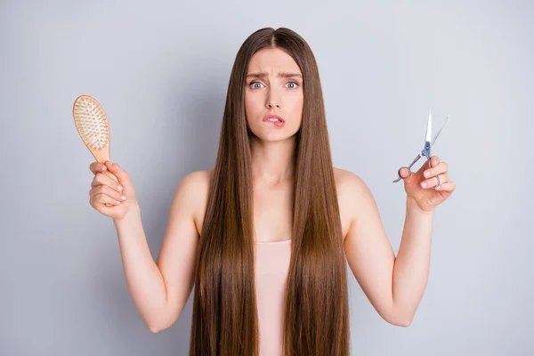 Foto de bela senhora assustada penteado longo segurar pente de madeira tesoura de metal tratamento profissional não tenho certeza sobre o corte de cabelo desgaste bege singlet isolado cor cinza fundo — Fotografia de Stock