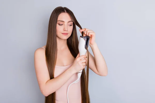 Foto van mooie model dame lang kapsel houden elektrische styler krulspelden maken rechte krullen golvend horloge resultaat dragen beige singlet geïsoleerde grijze kleur achtergrond — Stockfoto