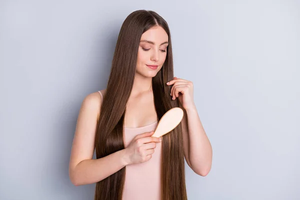 Foto van vreedzame aantrekkelijke model dame look lang kapsel houden favoriete houten kam zorgvuldig borstelen sterke rechte krullen dragen beige singlet geïsoleerde grijze kleur achtergrond — Stockfoto