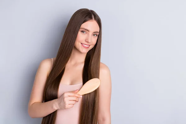 Foto von friedlichen attraktiven fröhlichen Modell Dame lange Frisur halten Lieblings-Holzkamm sorgfältig Bürsten starke Locken tragen beige Singlet isoliert graue Farbe Hintergrund — Stockfoto