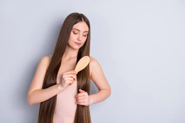 Foto von friedlichen attraktiven Modell Dame lange Frisur halten Lieblings-Holzkamm sorgfältig Bürsten starke erstaunliche Locken tragen beige Singlet isoliert graue Farbe Hintergrund — Stockfoto