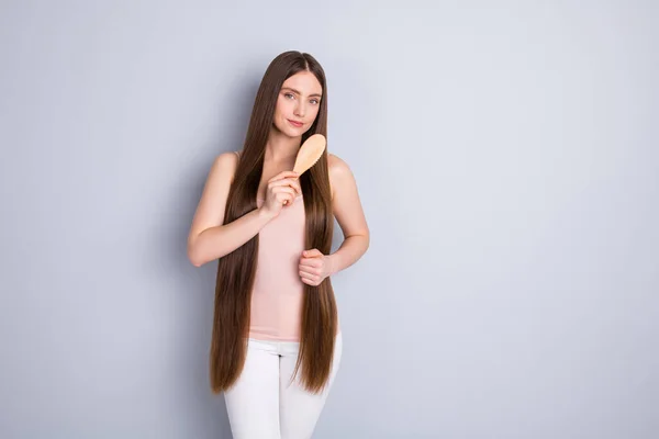 Foto av attraktiva perfekt utseende modell dam lång frisyr hålla favorit trä kam borsta starka lockar bära beige singlet byxor isolerad grå färg bakgrund — Stockfoto