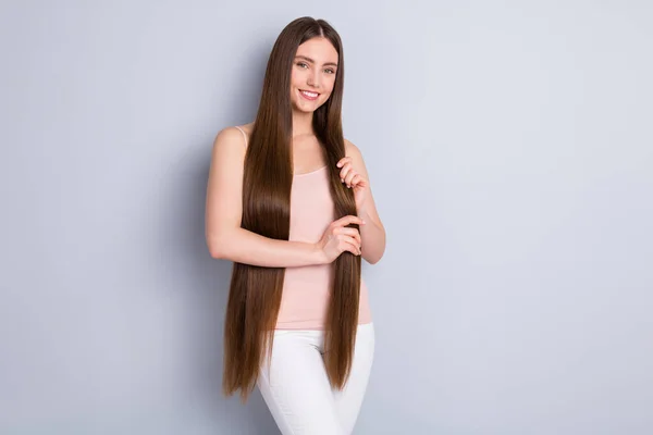 Foto de atractiva dama dentada poniendo máscara de seda líquida en ideal limpio largo sano peinado perfección cuidado del cabello vestido beige singlet pantalones blancos aislados color gris fondo — Foto de Stock