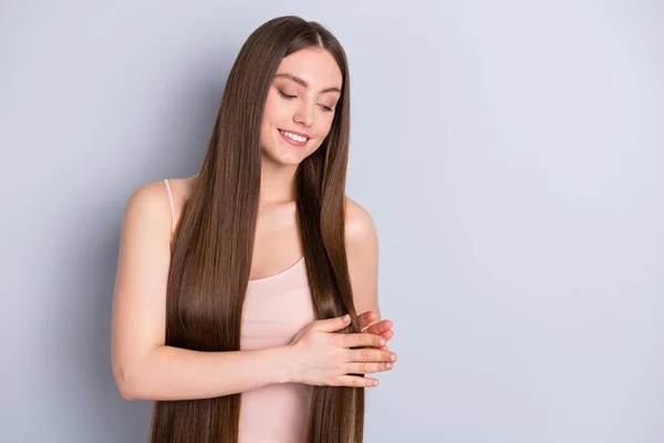 Foto van verbazingwekkende perfecte uitstraling model dame stralende glimlach zetten vloeibare zijde op ideale nette lange gezonde kapsel slijtage beige singlet geïsoleerde grijze kleur achtergrond — Stockfoto