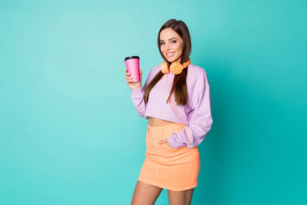 Zdjęcie uroczej pani trzymać papier kawa napój kubek słuchać nowoczesnej technologii słuchawki nosić przycięte fioletowy sweter nagi brzuch pomarańczowy spódnica izolowane ciemny kolor tła — Zdjęcie stockowe