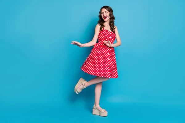 Full length photo of attractive pretty curly lady good mood flirty raise leg hands dancing look side wear summer red white dotted retro dress open toes shoes isolated blue color background — Stock Photo, Image