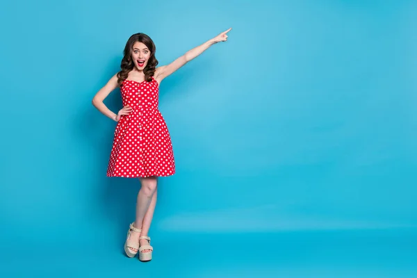 Full length photo of attractive lady hold arm direct finger far away traveler showing way excited mood wear red white dotted retro dress summer open toe shoes isolated blue color background — Stock Photo, Image