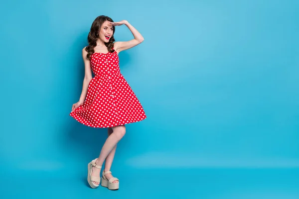 Фотография в полный рост привлекательной дамы блестит, улыбается, держит юбку, игривое настроение смотрит далеко, носит красное белое ретро-платье летние туфли с открытым носком на голубом фоне — стоковое фото