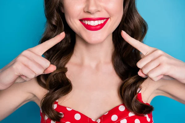 Closeup cropped photo of pretty lady toothy beaming smile directing finger mouth teeth after whitening procedure wear red dotted dress singlet isolated blue color background
