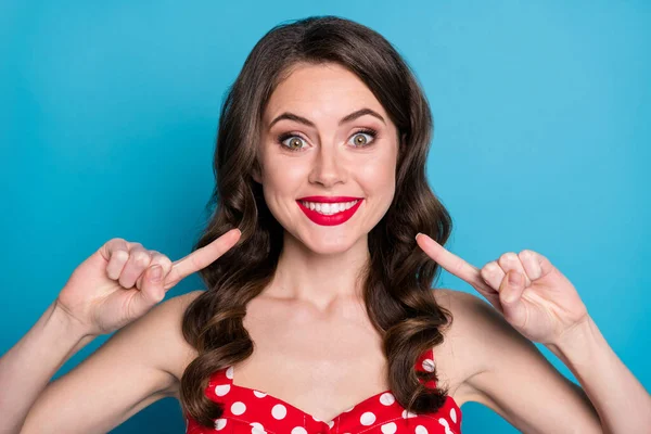 Closeup photo of pretty funny wavy lady toothy beaming smile directing finger mouth white bleaching teeth whitening procedure wear red dotted dress singlet isolated blue color background