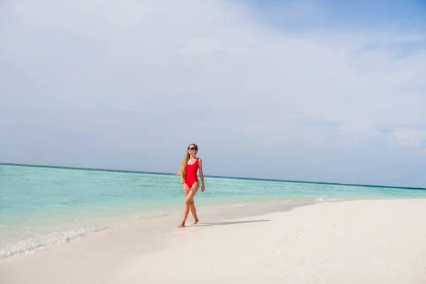 Full Size Profilfoto der schönen Dame lange Haare Spaziergang blau Wasser sinnlich schlanke Figur exotischen Ort leer Küste tragen Sonnenbrille roten Body genießen Sonnenstrahlen Meer Wellen Strand draußen — Stockfoto