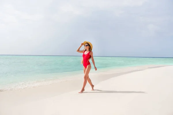 美しいスレンダーな女性の完全な長さの写真長い髪歩くだけ海岸砂のステップセクシーなフィギュア形エキゾチックなリゾートウェア太陽の帽子赤いボディスーツは外の太陽線海のビーチをお楽しみください — ストック写真