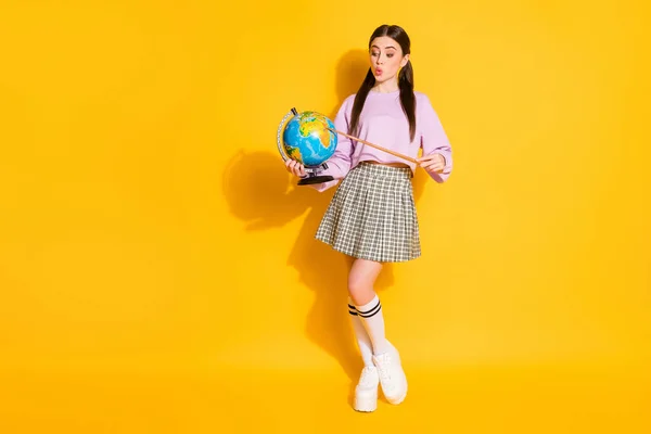 Full size photo of cute pretty brown school girl hipster hold globe point pointer continent impressed wear style stylish plaid pink white jumper isolated bright shine color background — стоковое фото