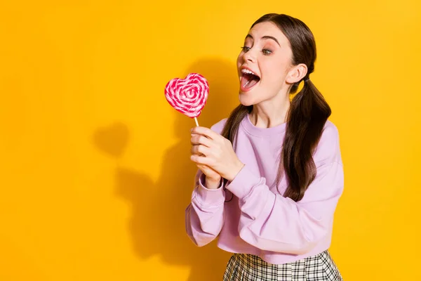 Πορτρέτο του θετικού χαρούμενα έφηβος κορίτσι θέλουν σνακ δοκιμάστε δάγκωμα καρδιά σχήμα καραμέλα φορούν καλή εμφάνιση καρό πουλόβερ απομονώνονται σε φωτεινό φόντο χρώμα — Φωτογραφία Αρχείου