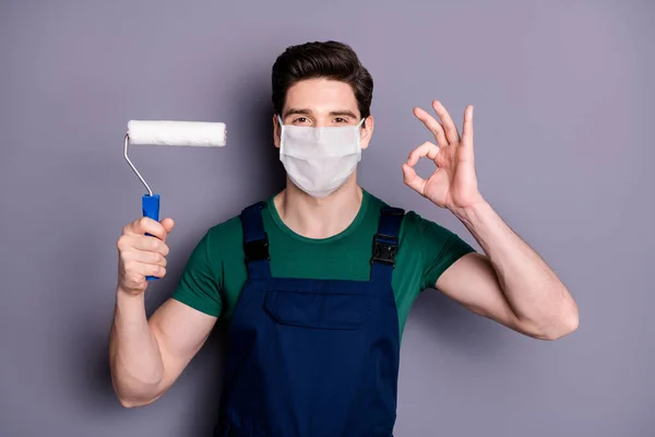 Close-up portret van zijn hij aantrekkelijke gezonde man schilder dragen veiligheid katoen masker mers cov influenza infectie preventie tekening muur gebouw tonen ok-teken geïsoleerde grijze kleur achtergrond — Stockfoto