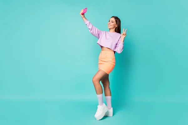 Ganzkörper-Foto von cool lady youth outfit halten telefon hände machen selfies zeigen v-sign symbol tragen abgeschnittenen pullover orange rock schuhe lange socken isoliert teal farbe hintergrund — Stockfoto