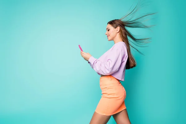 Profil foto av cool glad dam hålla telefon händer promenad gata skriva meddelande vänner njuta våren varm bris slitage beskärda pullover orange kjol isolerad teal färg bakgrund — Stockfoto