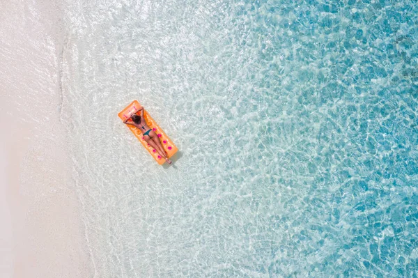 Yüksek açılı, havadan drone görüntüsü ince, sportif, çekici, kauçuk şilte üzerinde yüzen, şeffaf okyanus suyunun keyfini çıkar. — Stok fotoğraf