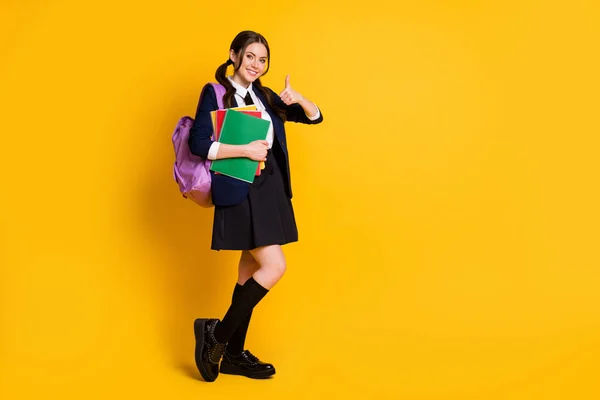 Longitud completa vista del tamaño del cuerpo de ella ella agradable atractiva colegiala alegre sosteniendo en la mano tema aprendizaje libro mostrando pulgar aislado en brillante brillo vivo vibrante color amarillo fondo —  Fotos de Stock