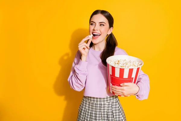 Портрет позитивной веселой девушки наслаждаться кино смотреть есть большой поп-кукурузной коробке носить клетчатый пуловер изолированы над блеском цвета фона — стоковое фото