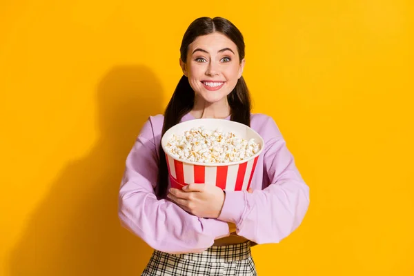 Porträtt av uppriktig rolig galen tonåring flicka hålla omfamna stora popcorn box medan du tittar på serien bära rutig pullover isolerad över ljusa glans färg bakgrund — Stockfoto