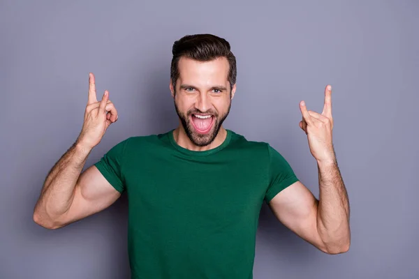 Zdjęcie atrakcyjny przystojny brodaty facet podnieść ręce pokazując co rogi symbole palce rocker wizyta zespół wydajność nosić casual zielony t-shirt odizolowany szary kolor tła — Zdjęcie stockowe