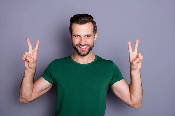 Fénykép a vonzó jóképű szakállas fickó emelje fel a kezét mutató v-jel szimbólumok ujjak köszönés barátoknak viselni alkalmi zöld póló elszigetelt szürke színű háttér — Stock Fotó