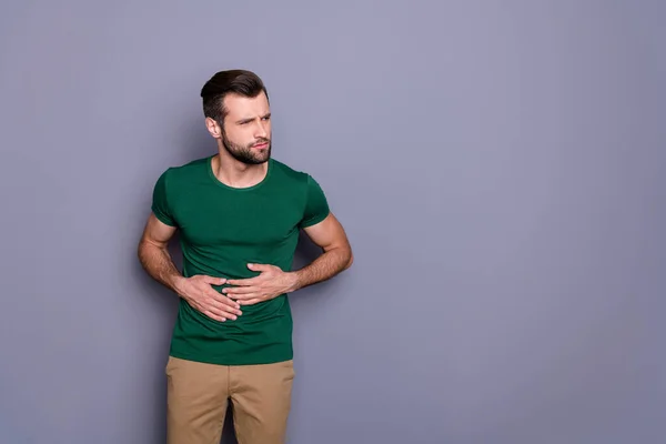Retrato de hombre frustrado comer algo mal sufrir dolor de estómago síndrome de gastritis usar pantalones verdes pantalones aislados sobre fondo de color gris — Foto de Stock