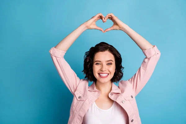 Photo of beautiful cheerful lady short black hairdo hold arms above head making heart figure shape dreamer express feelings wear casual pink jacket isolated blue color background — Zdjęcie stockowe