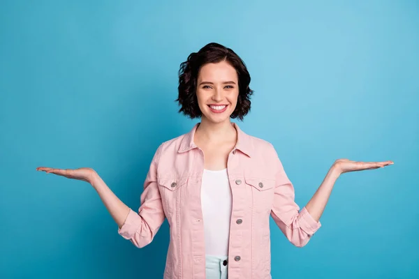 Photo of beautiful pretty lady short black hairdo hold open palms arms demonstrate advising two novelty sale price products select wear casual pink jacket isolated blue color background — Stock Photo, Image