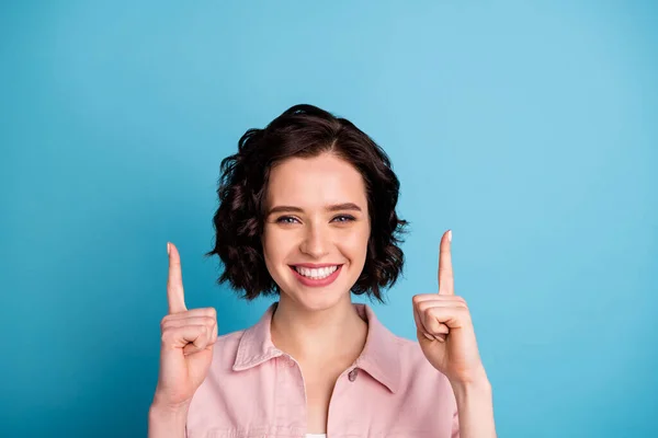 Close-up foto van aantrekkelijke dame kort zwart kapsel goed humeur direct vingers omhoog lege ruimte adviseren nieuwigheid product winkelen dragen casual roze denim jas geïsoleerde blauwe kleur achtergrond — Stockfoto