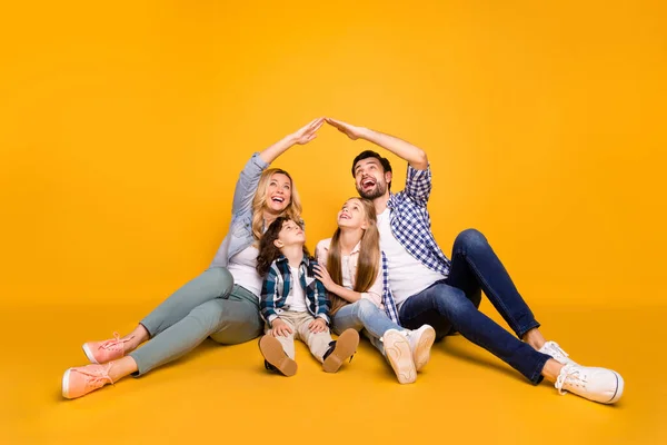 Foto mamá papá escuela niña hija pequeño hijo feliz juntos cuatro miembros familia seguridad cuidado concepto haciendo manos techo por encima de su cabeza aislado color amarillo fondo — Foto de Stock