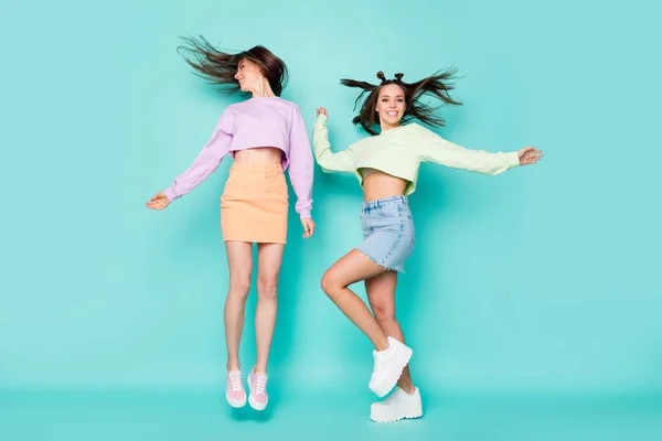 Helkroppsfoto av två ganska galna damer vänner hoppa upp ungdomskläder glädje dans party bära beskärda pullovers mini jeans kjolar skor isolerad pastell teal färg bakgrund — Stockfoto
