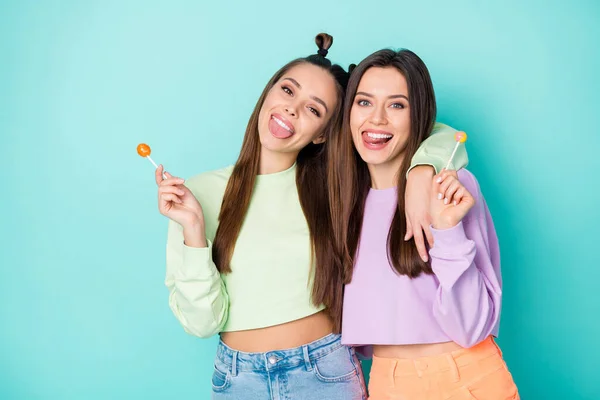 Photo of two funny crazy lady hold lollipop chupa chups hands sweets addicted stick tongue out mouth wear cropped pullovers naked belly skirts isolated pastel teal color background — Stock Photo, Image