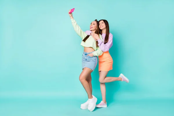 Helkroppsfoto av två glada damer hålla telefonen ta selfies sticka ut tungan bära beskärda tröjor naken mage korta kjolar skor isolerad pastell teal färg bakgrund — Stockfoto
