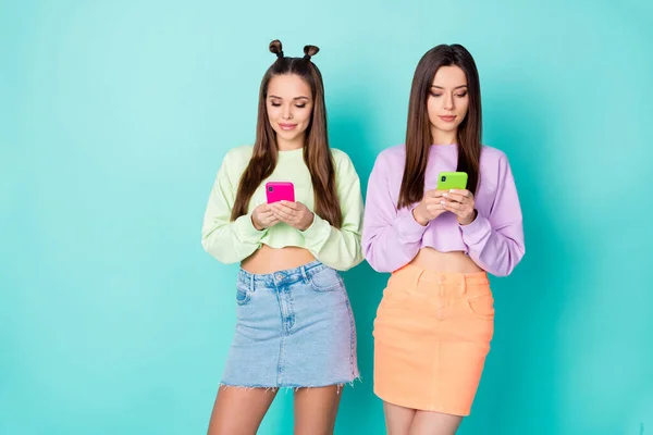 Foto van twee coole grappige zussen dames beste vrienden op zoek telefoon handen chatten elkaar dragen bijgesneden truien naakte buik korte rokken geïsoleerde pastel teal kleur achtergrond — Stockfoto