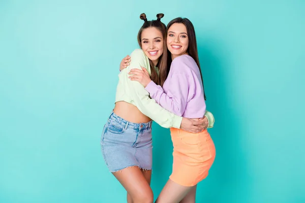 Foto de duas irmãs encantadoras senhoras amigos juventude olhar roupas roupa abraçando feliz em conhecer o outro usar camisolas cortadas barriga nua saias curtas isolado pastel teal cor fundo — Fotografia de Stock