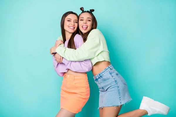 Photo of two cheerful ladies best friends cool youth look sticking tongue out mouth hugging wear cropped sweaters naked belly short skirts isolated pastel teal color background — Stock Photo, Image