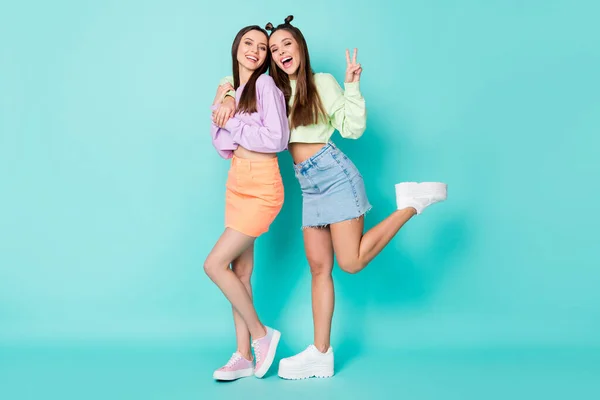 Full body photo of two cheerful ladies best friends cool look clothes hug show v-sign symbol wear cropped sweaters naked belly short skirts shoes isolated pastel teal color background — Stock Photo, Image