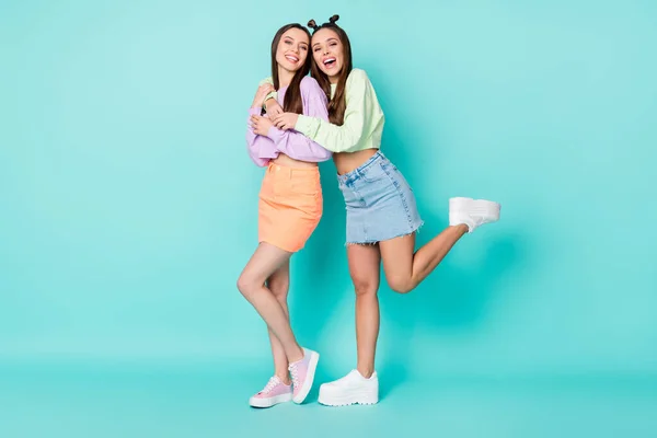 Full längd foto av två glada damer vänner cool look kläder kramar eleverna bära beskärda tröjor naken mage korta kjolar skor isolerad pastell teal färg bakgrund — Stockfoto