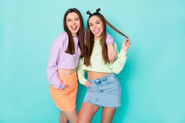 Photo of two cheerful lady best friends cool youth look sticking tongue out mouth crazy mood wear cropped sweaters naked belly short skirts isolated pastel teal color background — Stock Photo, Image