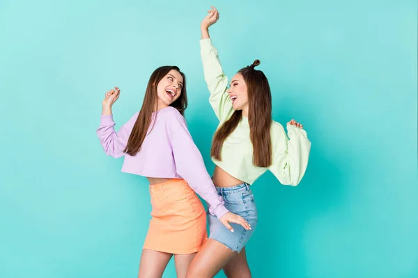Photo of two cheerful lady girlfriends celebrate student party cool clothes dance favorite song wear cropped sweaters naked belly short skirts isolated pastel teal color background — Stock Photo, Image